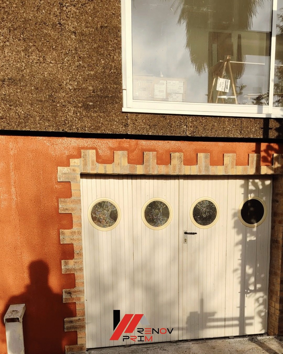 Porte de garage à hublots et encadrement brique sur façade enduit orange